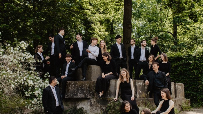 Eine formelle Gruppe von Musiker:innen, die sich gemeinsam im Freien in einer üppigen, grünen Parklandschaft fotografieren lässt.