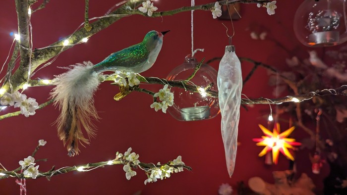 Ein bunter Vogel sitzt auf einem Weihnachtsbaumzweig mit Lichtern und Christbaumschmuck