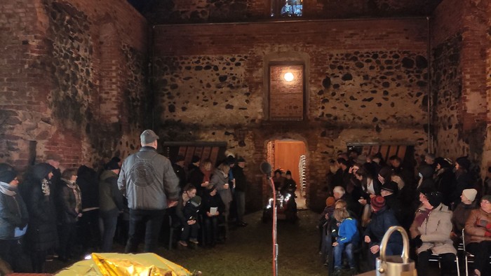 Gottesdienst in de Kirchenruine Lichtenberg. Ein beleuchteter Herrnhuter Stern, Menschen in warmer Kleidung, auf dem Altar eine brennende Kerze in einer Laterne.