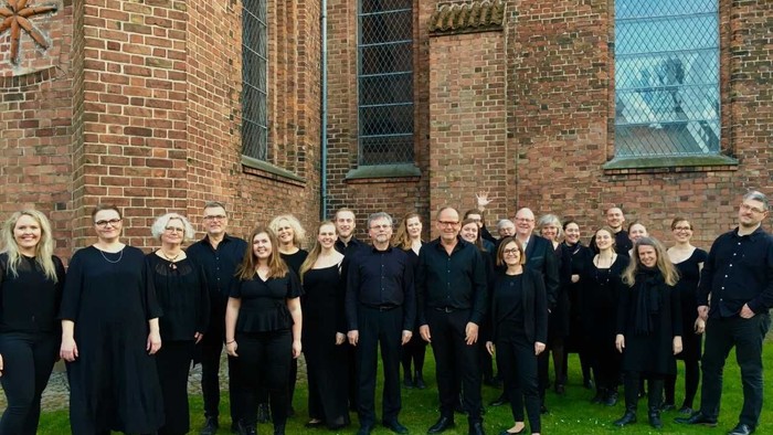 En gruppe af korister står sammen foran en murstenskirke.
