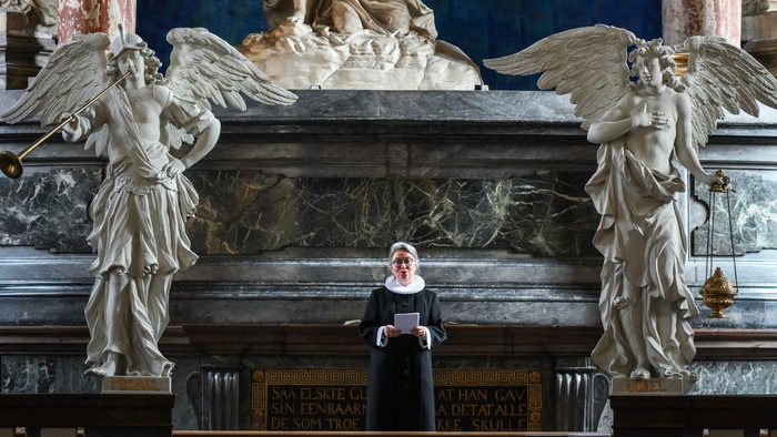 En præst står i en prægtig kirke med store skulpturer og malerier.