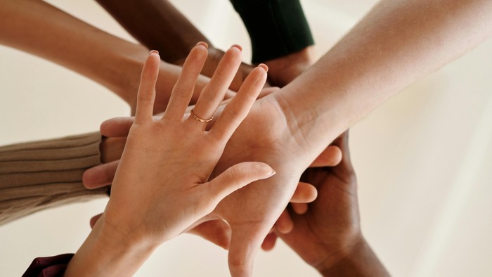 Viele Hände bilden einen Stapel, eine zeigt einen Ehering