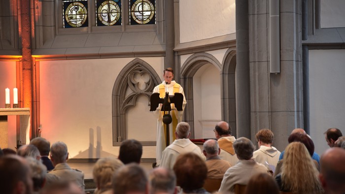 Ein Mann in Soutane predigt vor einer großen Menschenmenge in einer Kirche.