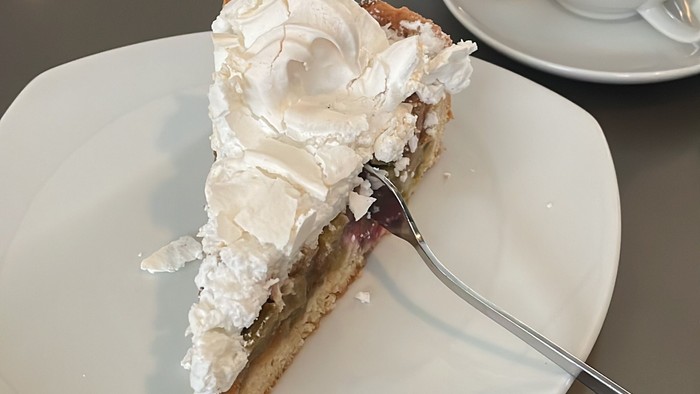 Ein Stück Kuchen auf einem Teller mit Gabel, daneben Teetasse und Zuckerdose