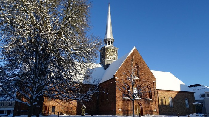 En snedækket kirke med tårn og klokke.