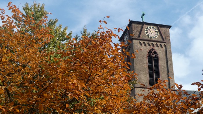 Herbstblätter vor Kirchturm mit Uhr