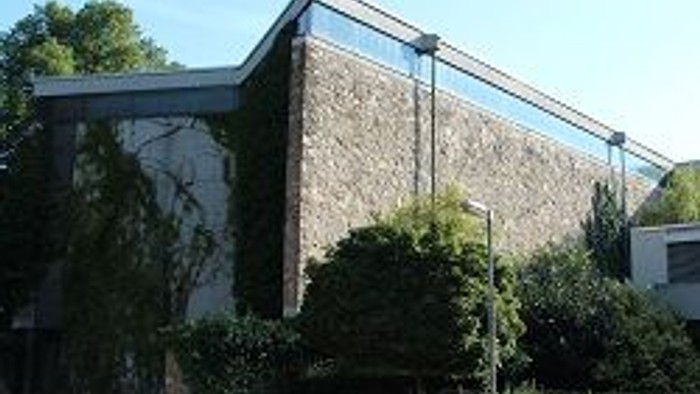 Das Bild zeigt ein modernes Gebäude mit Glasfront und umgeben von Grün.