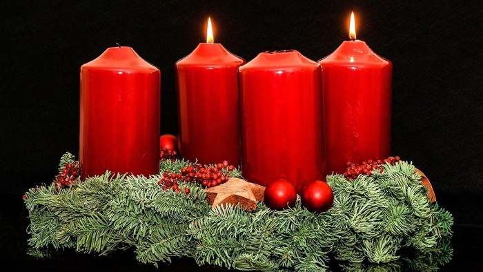 Vier brennende rote Kerzen auf grünem Kranz mit Weihnachtskugeln