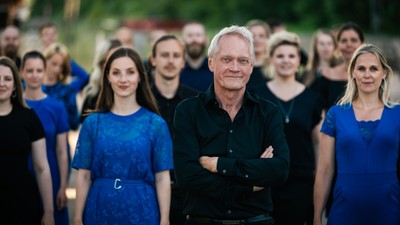 En gruppe af mennesker står sammen, hovedsageligt kvinder i blå og sorte klæder, med en ældre mand i midten.