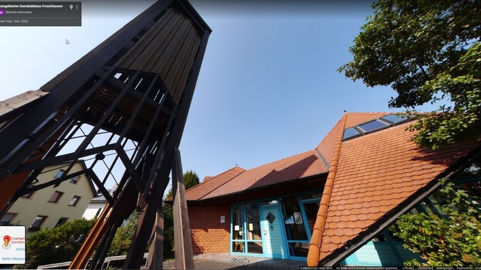 Eine große hölzerne Kranstruktur neben einem Gebäude mit rotem Dach und blauen Akzenten sowie Bäumen in der Nähe.