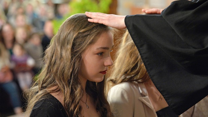 Konfirmand*innen werden durch eine Pfarrperson mit Handauflegen gesegnet.