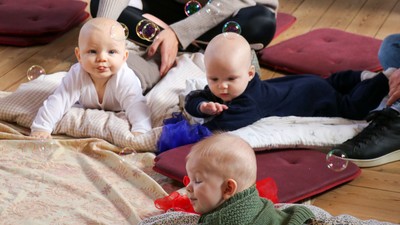 Tre små børn ligger på gulv med dekker og legetøj.
