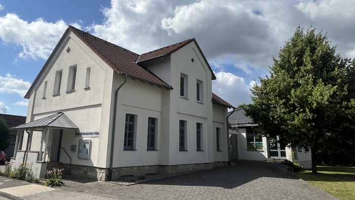 Das Bild zeigt das Laggenbecker Gemeindehaus, ein weiß verputztes Gebäude mit einem Anbau rechts.