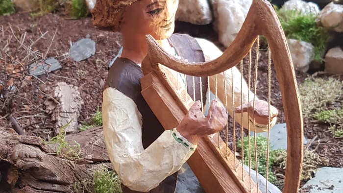 Eine kleine Figur spielt eine Harfe auf einem Felsen.