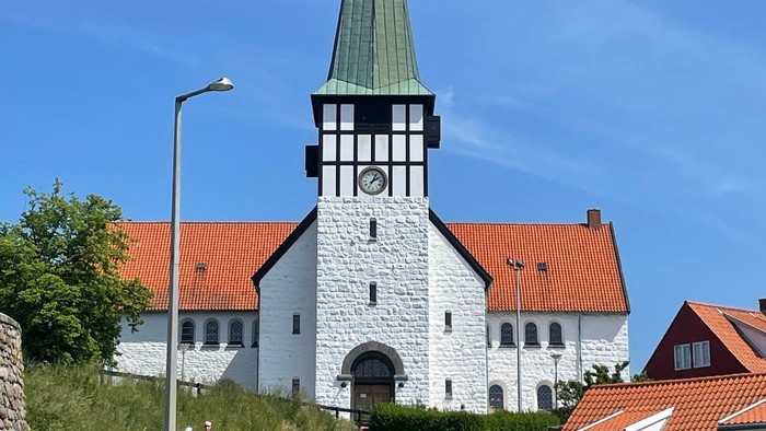 En hvid kirke med spiret og klokke, omgivet af andre huse med røde tag.