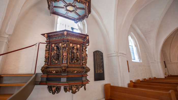 En prædikestol med udsmykning i en kirke med hvidt tagt.