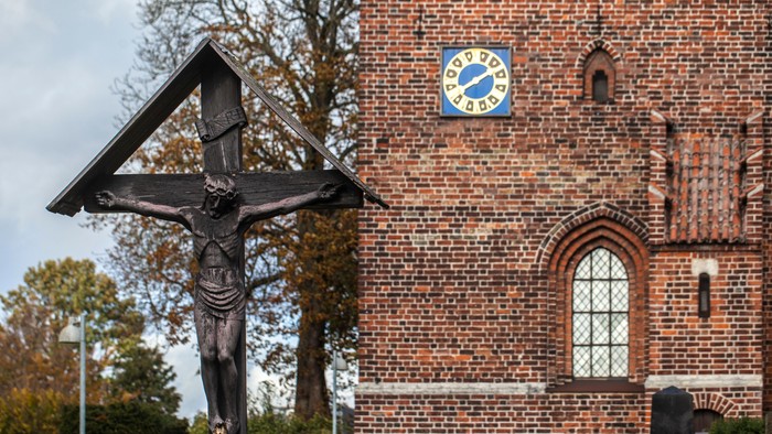 En kors med Jesus Kristus foran en murstenskirke med klokke.