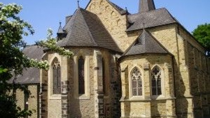Altes steinernes Kirchengebäude mit spitzen Bögen und Kreuz auf dem Dach.