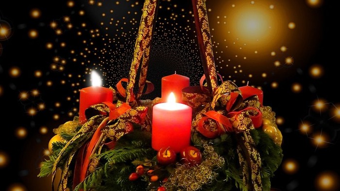 Ein Adventskranz mit vier brennenden Kerzen vor einem dunklen Hintergrund