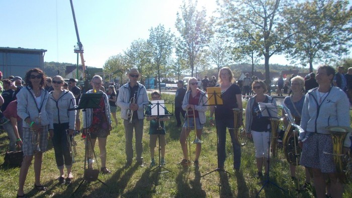 Eine Gruppe von Menschen steht im Freien und singt in Notenheften.