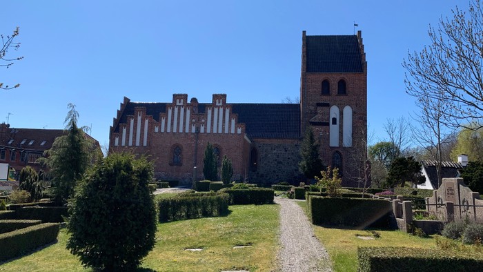 En stor, gammel kirke af røde mursten med en høj tårn i en trædet og grøn have