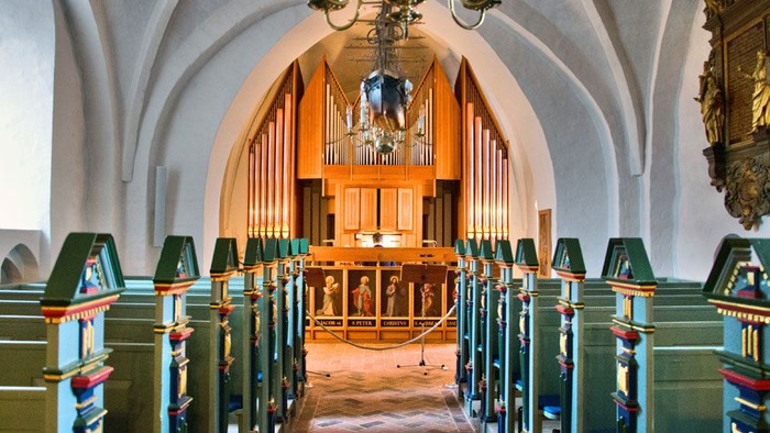 Innendørs billede af kirke med orgel og bænke.