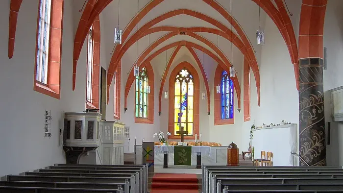 Kircheninneres mit roten Bögen, Buntglasfenstern und hölzernen Kirchenbänken.