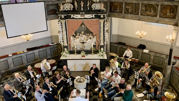 Ein Orchester probt in einem prächtigen Saal mit Zuschauerbalkon.