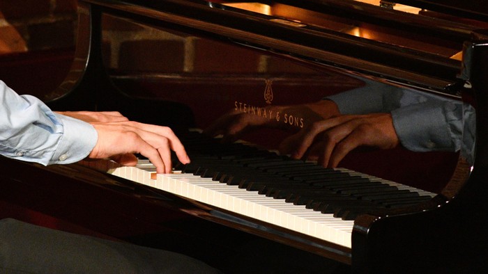 Hænder spiller piano på sort instrument