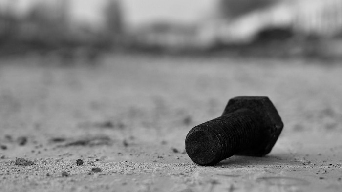 Ein Schraubenbolzen liegt auf einer staubigen Oberfläche.