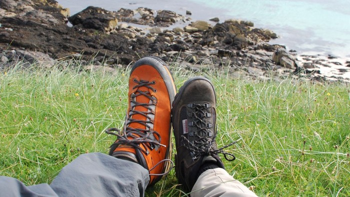 Beine mit Wanderschuhen auf einer grünen Wiese mit Felsen am Meer