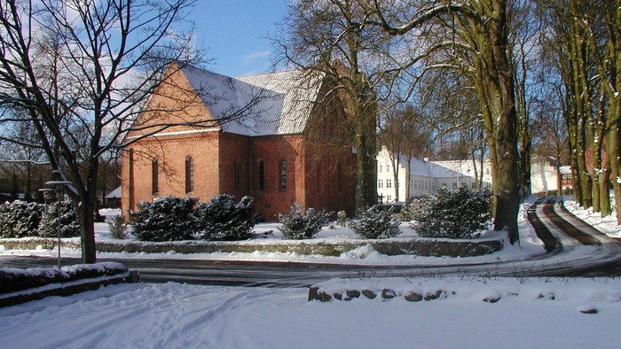 En rød murstenskirke med snede på taget og træer i sne.