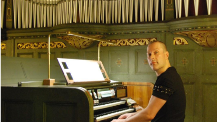 Mann spielt Orgel in einem prunkvollen Raum.