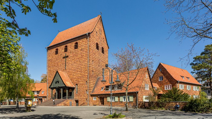 Das Bild zeigt eine Kirche mit hohem Turm und rotem Dach, umgeben von Bäumen und anderen Gebäuden.