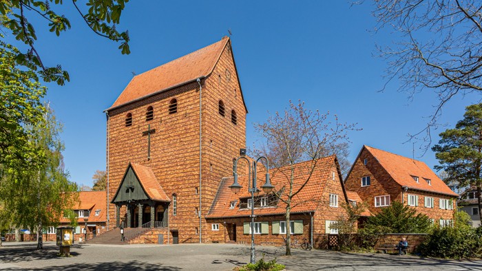 Das Bild zeigt eine Kirche mit hohem Turm und rotem Dach, umgeben von Bäumen und anderen Gebäuden.