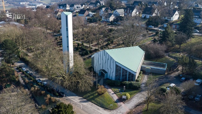 Das Bild zeigt eine moderne Kirche mit hohem Turm in einem Vorort.