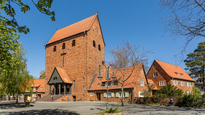 Das Bild zeigt eine Kirche mit hohem Turm und rotem Dach, umgeben von Bäumen und anderen Gebäuden.