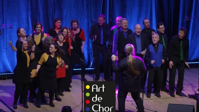 Ein Chor tritt auf einer Bühne auf, begleitet von einem Dirigenten