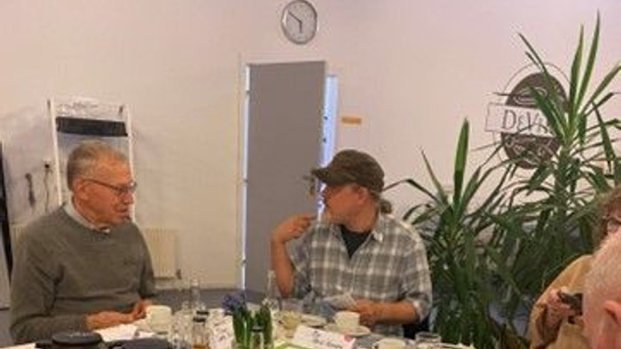 En gruppe mennesker sidder ved et bord med kage og teetøj.