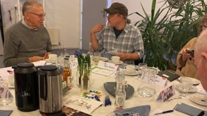 En gruppe mennesker sidder ved et bord med kage og teetøj.