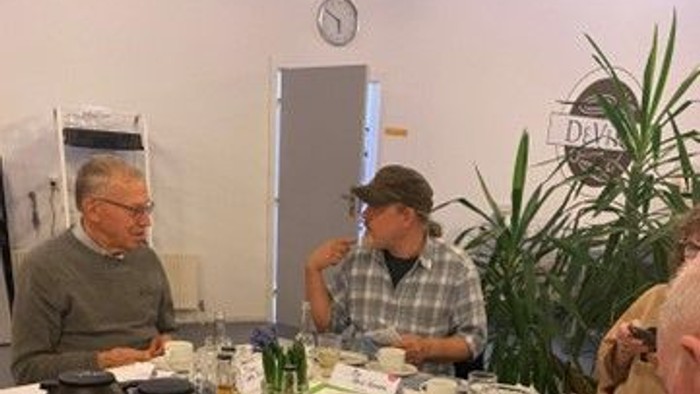 En gruppe mennesker sidder ved et bord med kage og teetøj.