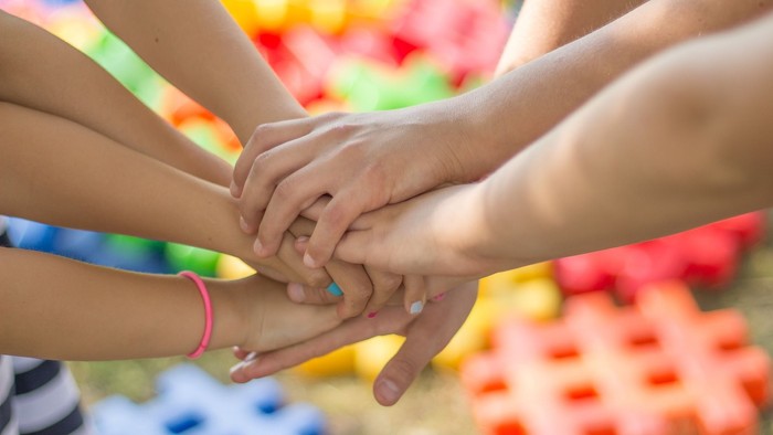 En gruppe af hånders håndflader sammen på en farverig overflate.