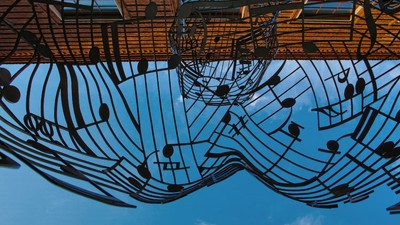 Ein modernes Metallskulptur mit Notenlinien und Tönen vor einem blauen Himmel.