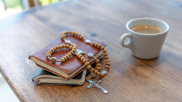 Ein Holztisch mit Büchern, Rosenkranz und Kaffeetasse
