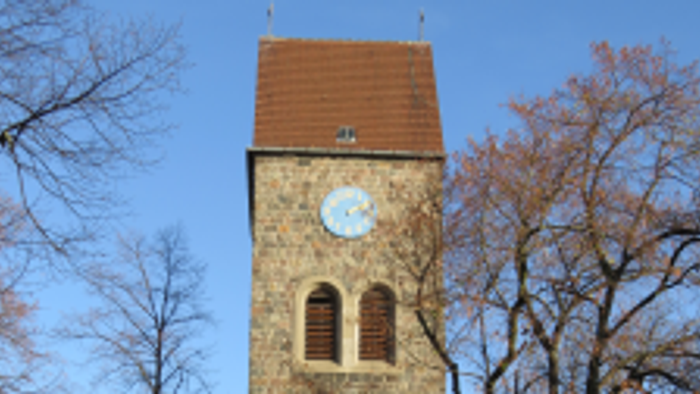 Alter Kirchturm mit Uhr und buntem Glasfenster, umgeben von Bäumen