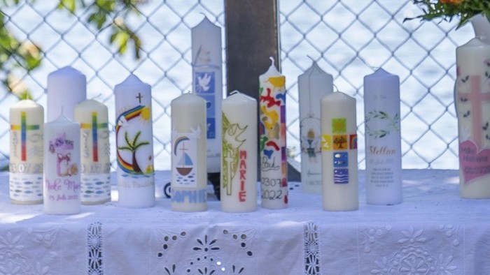 Ein Tisch mit weißer Tischdecke, darauf ein großes Holzkreuz und mehrere Kerzen in verschiedenen Farben