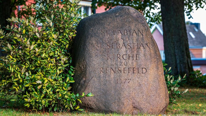 Stein mit Inschrift im Garten, Haus im Hintergrund