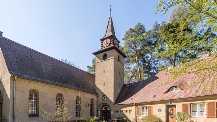 Kirchengelände mit Uhrturm und Nebengebäuden, umgeben von Bäumen