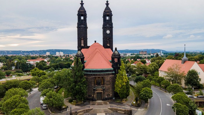 Zwei Kirchtürme mit roter Kuppel inmitten von Bäumen und Gebäuden.