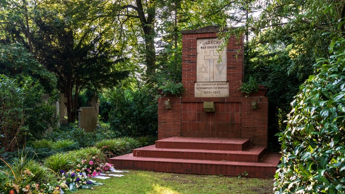 Ein Gedenkstein aus Backstein in einem grünen Park mit Treppe und Blumen.